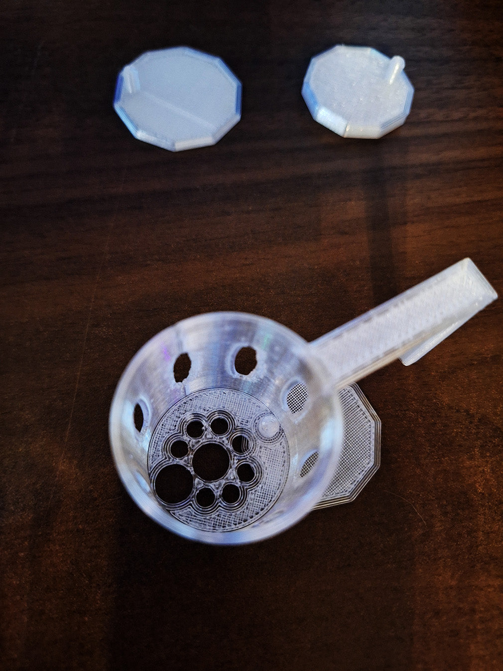 Top view of a Hang-On Plant Buddy, printed in Overture Translucent PETG, designed for rimmed tanks with a unique leveler to maintain stability. Also shown are two hexagonal levelers, all set against a rich wooden surface.