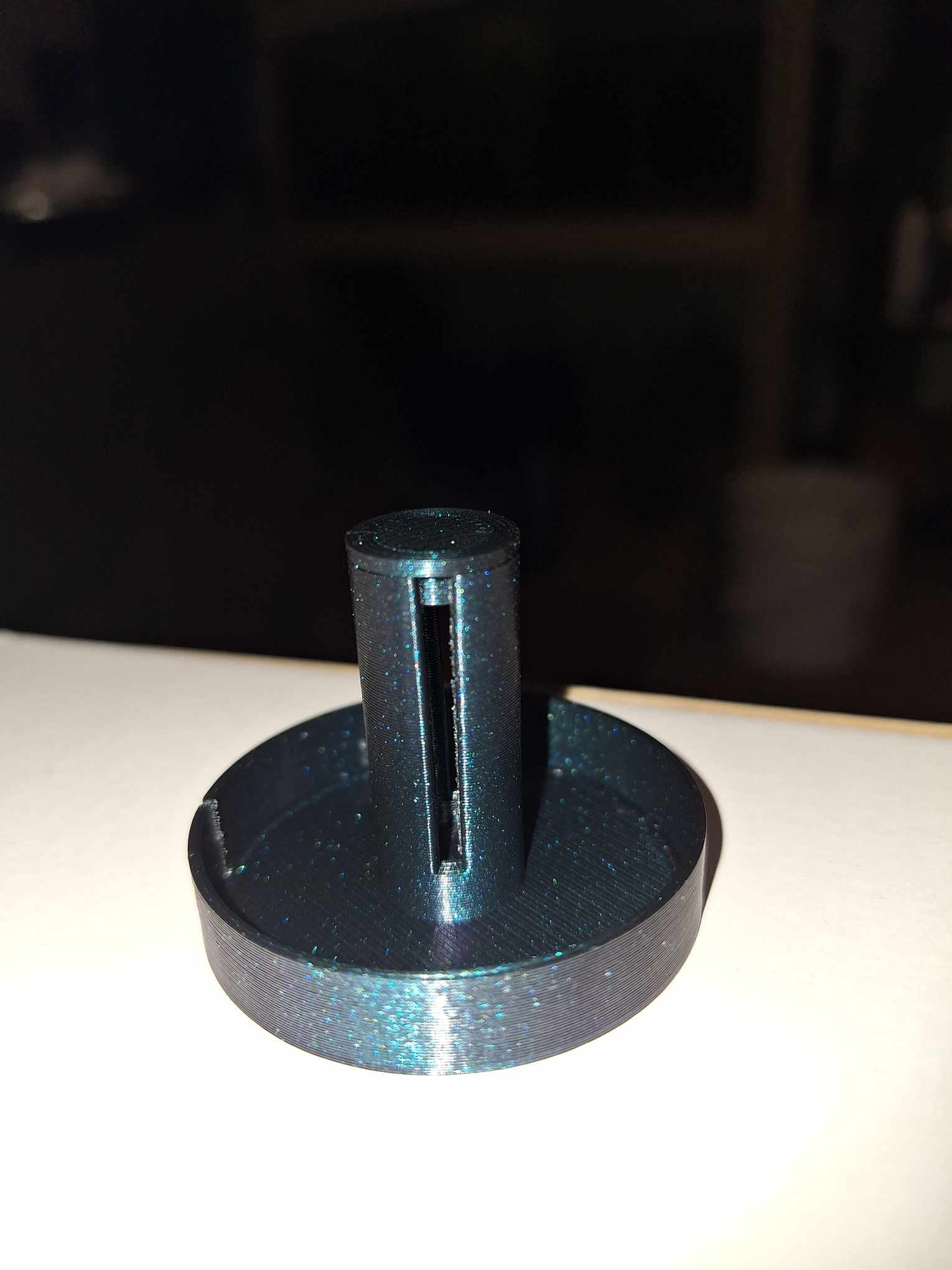 A sleek Snail Saver Trap made from Flashforge Burnt Titanium PETG, featuring a shimmering, cylindrical design with a central slit, displayed against a dimly lit background for a clear view of the product.