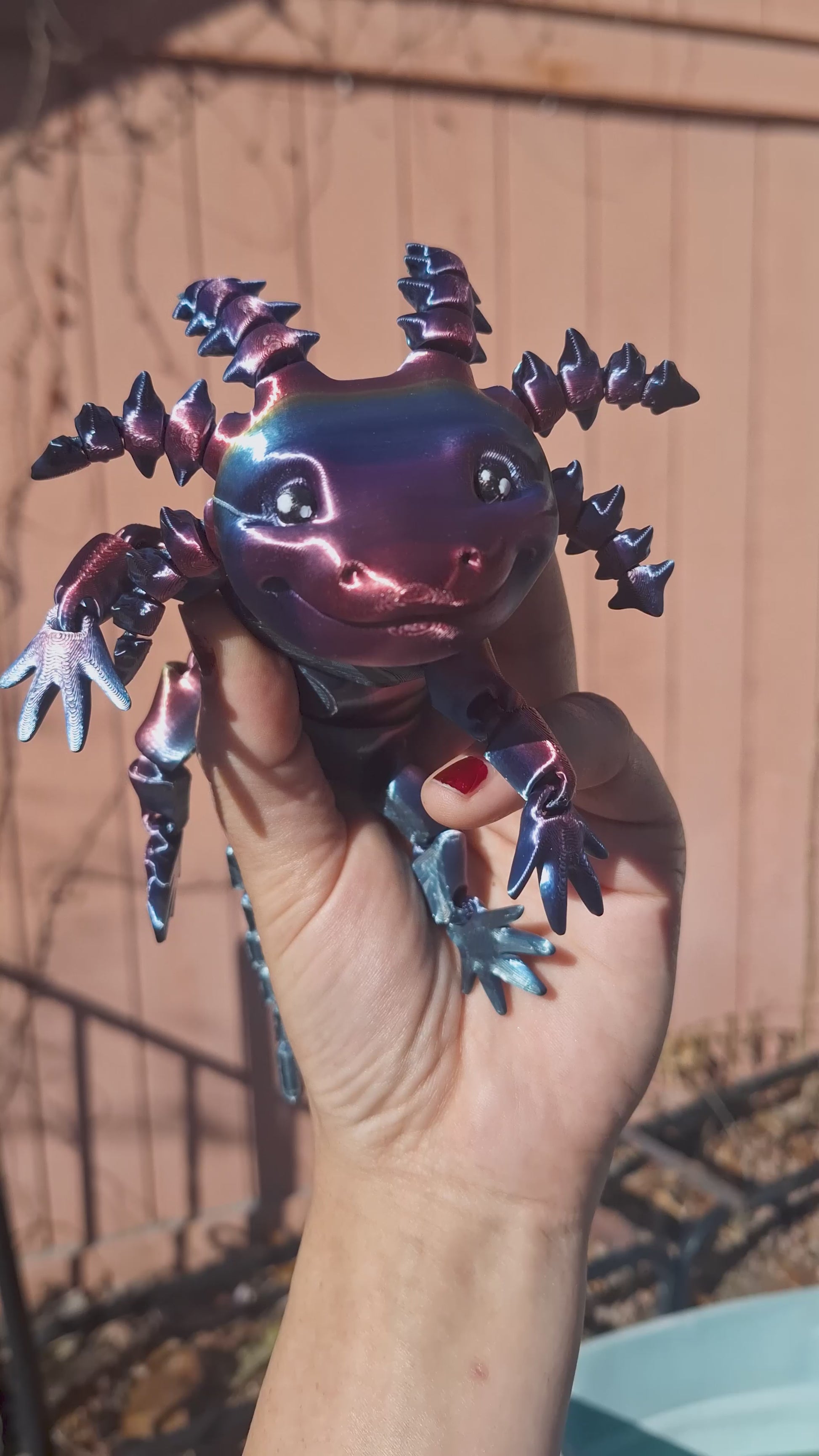 A hand holding the 3D printed Articulated Axolotl Redux, demonstrating the articulating movement of the arms, gills, legs, and tail