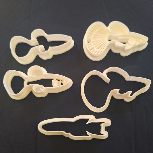 Set of five food-safe Creality White PLA guppy-shaped cookie/clay cutters, each featuring a unique design, displayed on a black background.