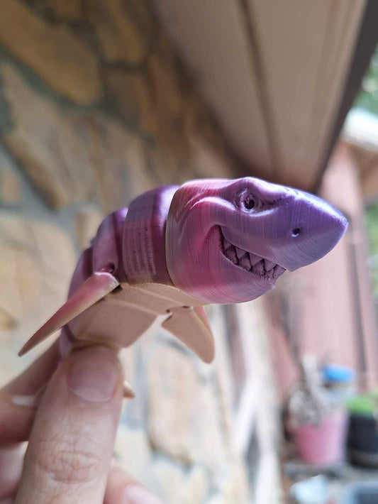 Articulated Great White Shark model held in hand, printed with Eryone Silk PLA in Rainbow Candy colors, featuring a gradient from purple to pink, with a focused and detailed facial expression against a blurred outdoor background.