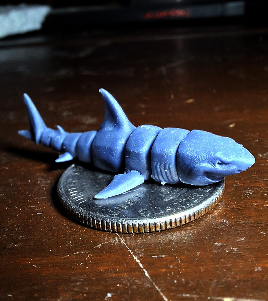 A tiny 3D-printed model of a Great White Shark in ABS-like resin, perched atop a quarter to demonstrate its miniature size, from the 'Tinies' line by Cassie's Critters and Creations. Model design by MatMireMakes.