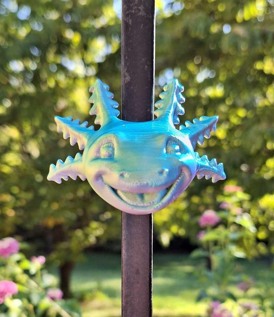 Vibrant Big Smile Axolotl magnet 3D-printed with Aceaddity Blue/Yellow/Purple tri-color silk PLA, attached to a metal rod with a lush garden background. The playful axolotl design features a cheerful expression and a smooth, silk-like finish, perfect for animal lovers and quirky home decoration.