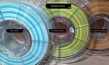 3 spools of filament with gradient colors. From left to right - Winter (white to blue), Matcha (matte yellow to green to brown), and Wood Grain (matte dark brown to tan).