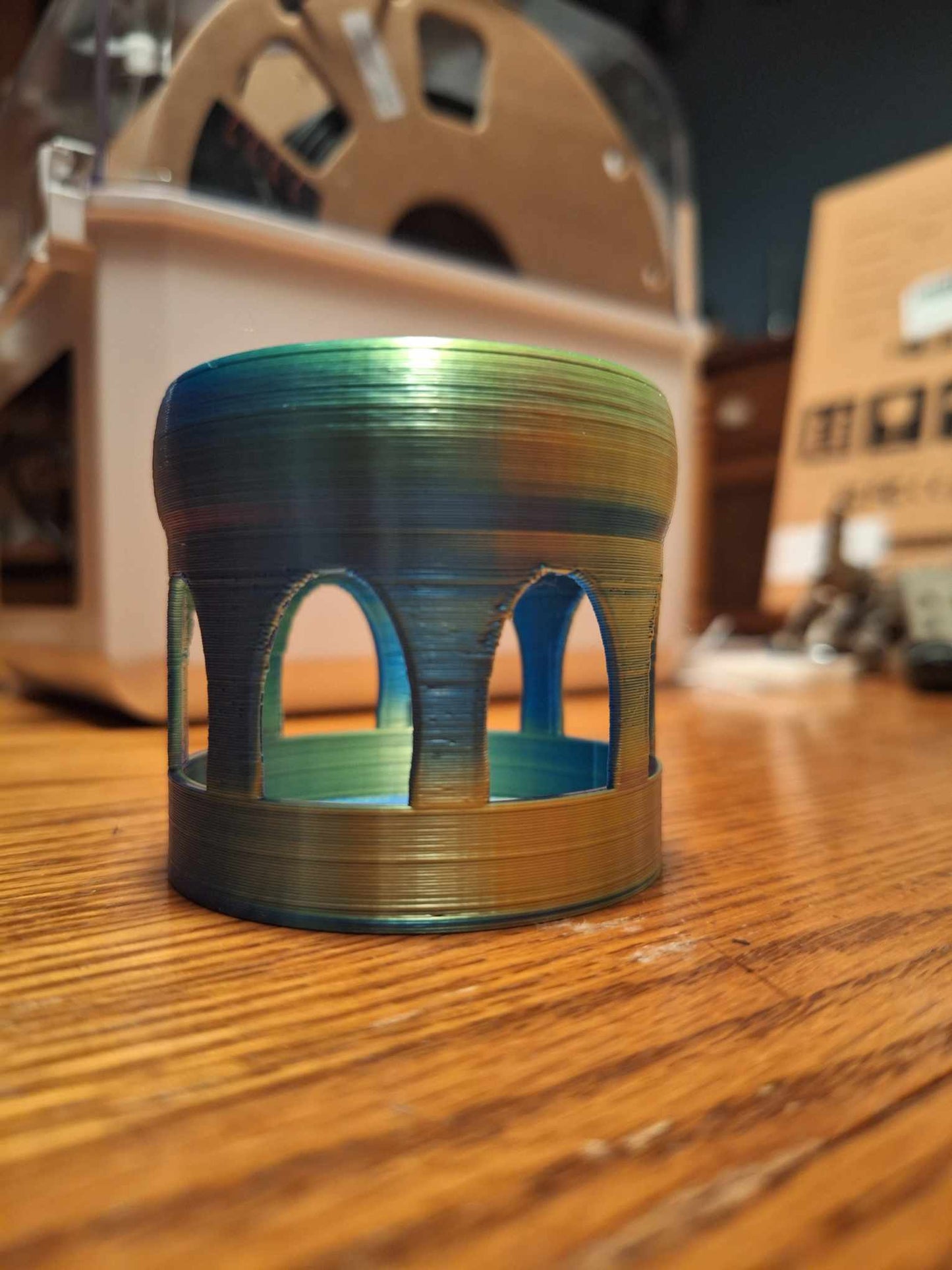 Strikingly colorful Floating Shrimp Gazebo Feeder 3D-printed with Aceaddity tri-color silk PLA in shades of blue, yellow, and purple, placed on a wooden surface with a Sovol filament dryer in the blurry background.