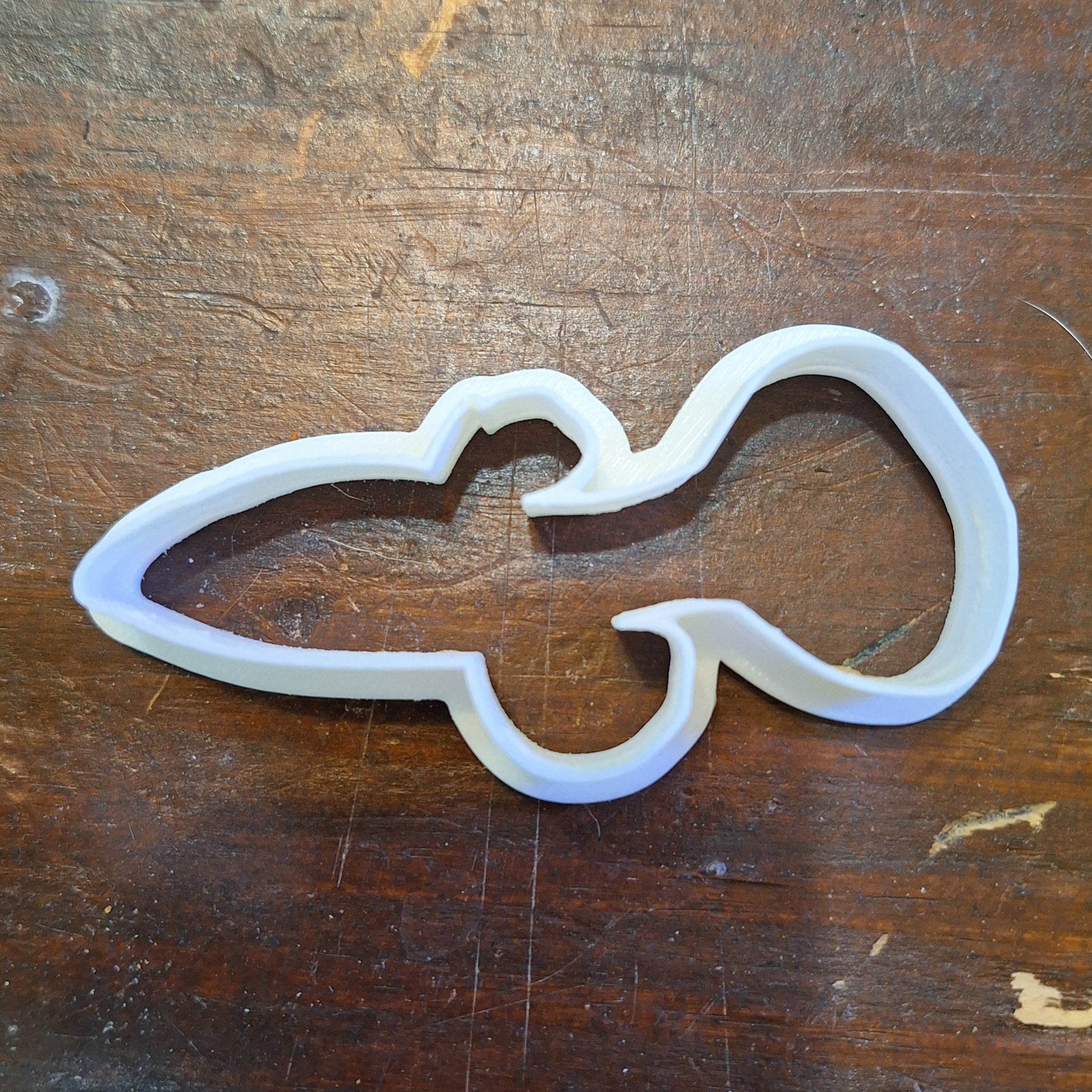 Standard guppy-shaped cookie/clay cutter in Creality White PLA, showcasing a simple and sleek design, against a worn wooden backdrop