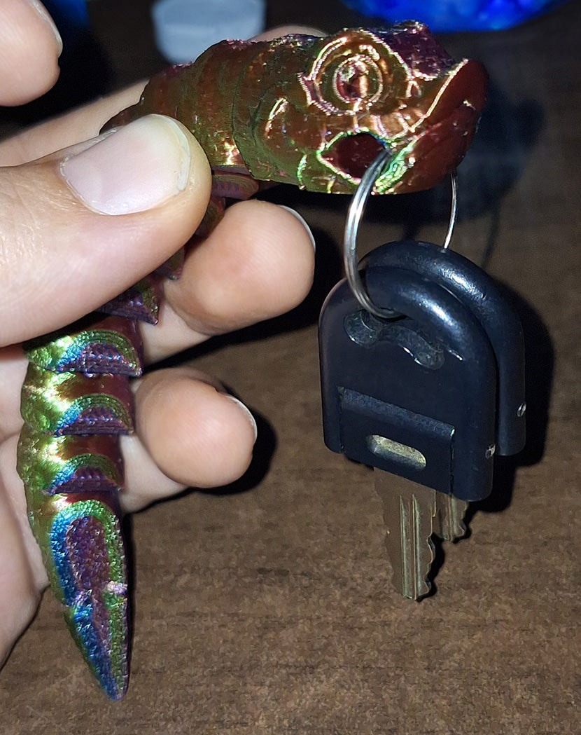 Hand holding an articulated hognose keychain, printed in Eryone Silk PLA with an iridescent sheen of red, blue, and green. The keychain's segments are flexibly connected, providing tactile feedback with each movement. Attached to a set of keys, this keychain combines functionality with a sensory experience, making it an attractive accessory for personal use and tactile fidgeting.