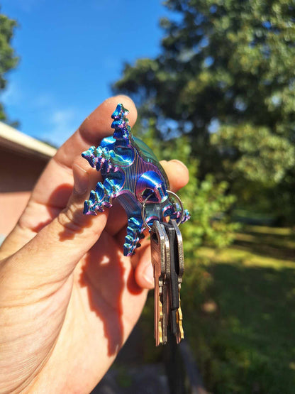 Hand holding a Big Smile Axolotl keychain, 3D-printed with Aceaddity Blue/Red/Green tri-color silk PLA, showcasing vibrant color shifts and a glossy finish. The keychain is hooked to a set of keys, with a clear blue sky and greenery in the backdrop, perfect for enthusiasts of unique accessories and amphibian-themed items.