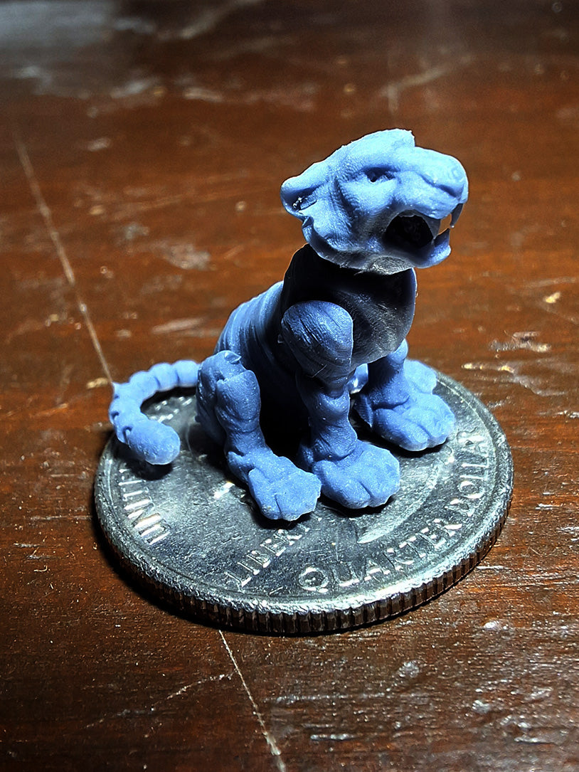 A tiny 3D-printed model of a Roaring Tiger in ABS-like resin, perched atop a quarter to demonstrate its miniature size, from the 'Tinies' line by Cassie's Critters and Creations. Model design by MatMireMakes.