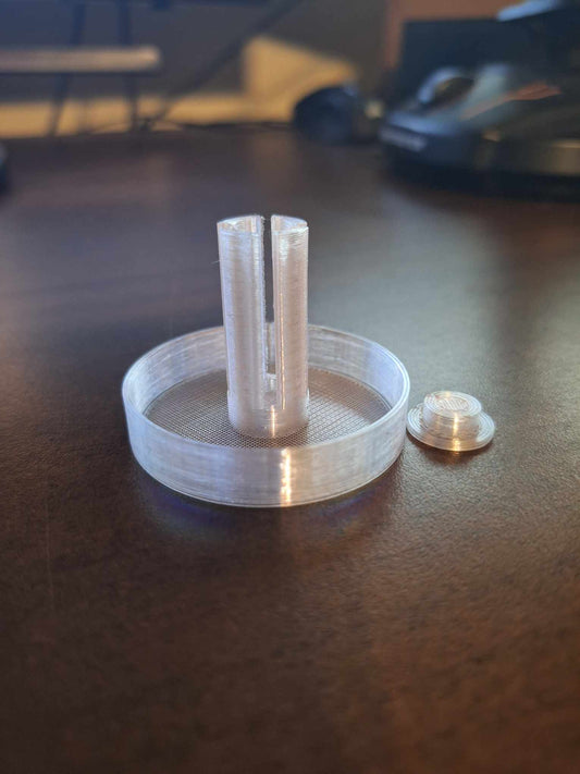 Overture Translucent PETG Snail Saver Trap placed on a desk with its lid beside it, demonstrating the clarity and quality of the material. The trap's semi-transparent design allows for easy monitoring of snails within a sleek, modern appearance.