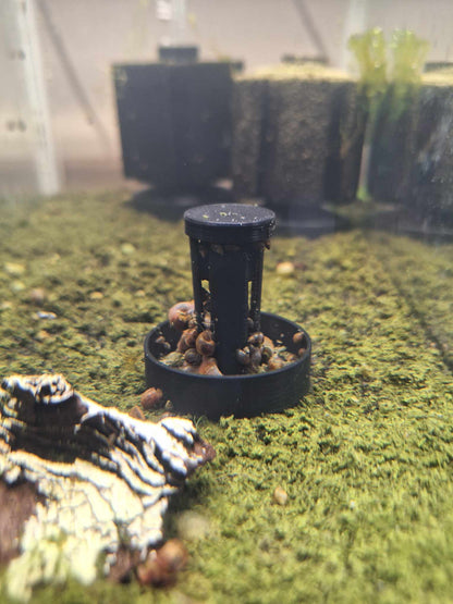 End of the timelapse: Overture black PETG Snail Saver Trap with snail bait inside. There are many snails in the trap and all over the bait tube, set in an aquarium environment with detritus and snail waste.