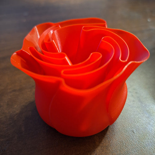 Vibrant red 3D-printed rose with space for an electronic tealight, designed to mimic the intricate layers of petals, displayed on a dark surface.